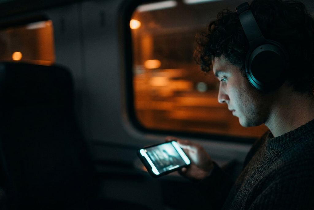 A person in headphones on a night train, watching a film frame on a phone.